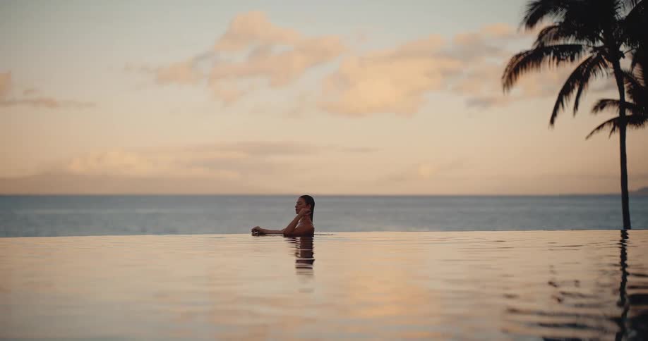 Woman relaxes in a luxurious infinity pool, enjoying a tranquil and beautiful sunset over the ocean