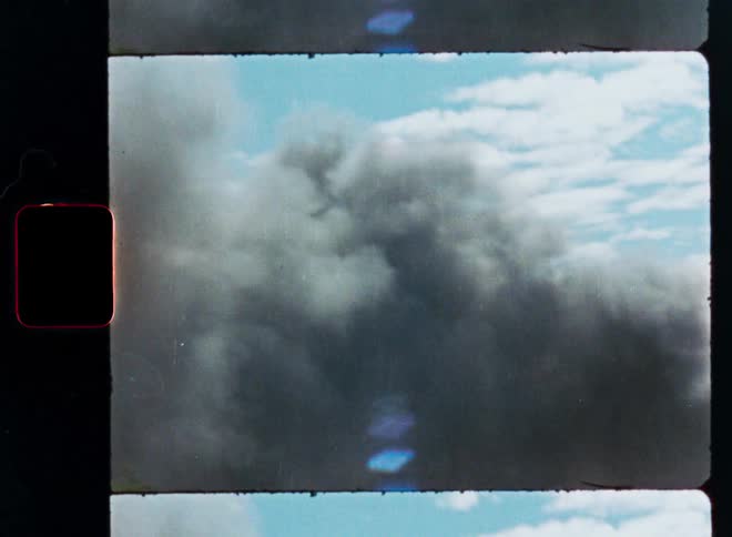 Vintage film scan shows a thick, dark plume of smoke rising into a blue sky