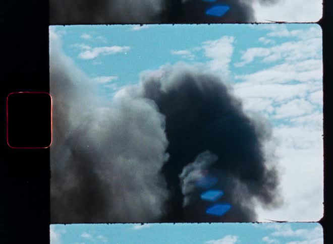 Vintage 8mm film footage captures a thick, dark plume of smoke billowing into the bright blue sky