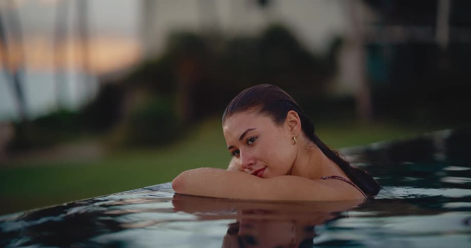 A beautiful woman relaxes in an infinity pool at a luxury resort during a tropical sunset