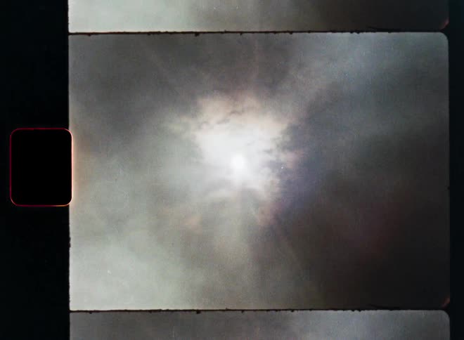 An authentic 8mm film scan captures a dreamy time-lapse of the sun emerging from behind dark, moody clouds