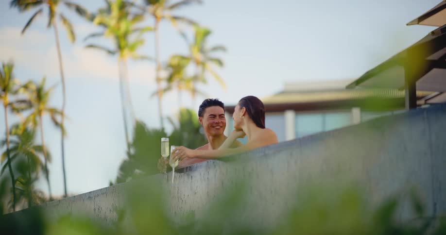 An attractive couple enjoys a romantic conversation while sipping champagne and relaxing in a luxurious resort swimming pool