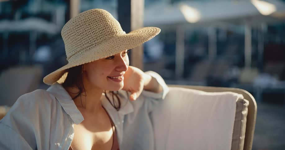 Portrait of a smiling woman in a summer hat relaxing on a sun lounger at a luxury resort during sunset