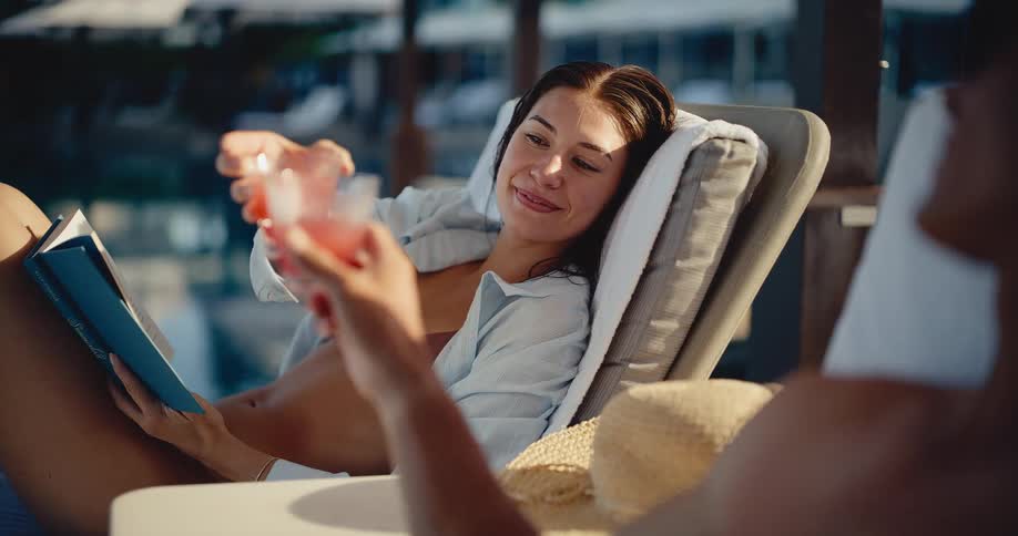 Happy young couple toasts with cocktails while relaxing on lounge chairs by the pool at a luxury resort