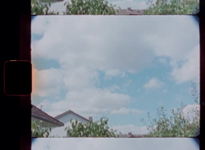 Vintage 8mm film captures a slow upward pan from a suburban garden to the cloudy blue sky