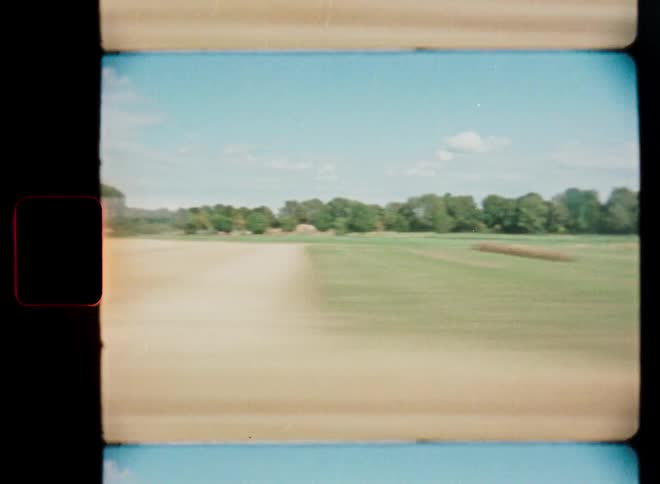 Vintage Super 8 film captures a blurry, fast-moving shot of a wide open field and treeline from a moving vehicle