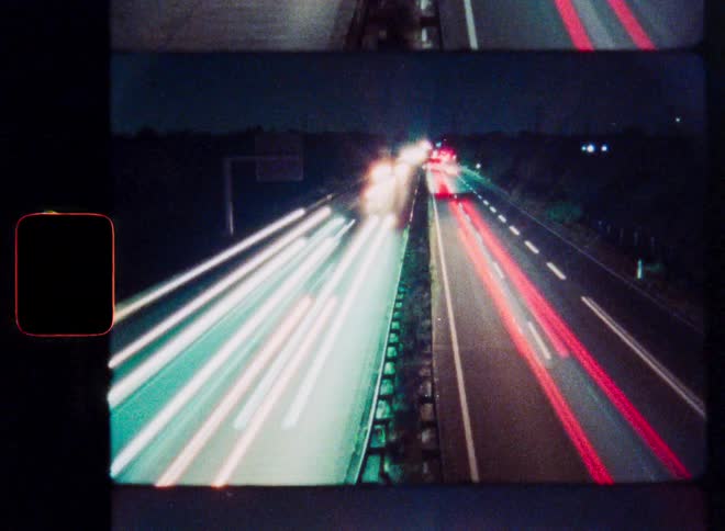 An abstract analog film time-lapse shows light trails from cars speeding down a highway at night