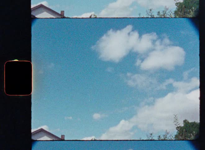 A slow upward pan from a suburban backyard to a blue sky with white clouds, shot on grainy vintage film