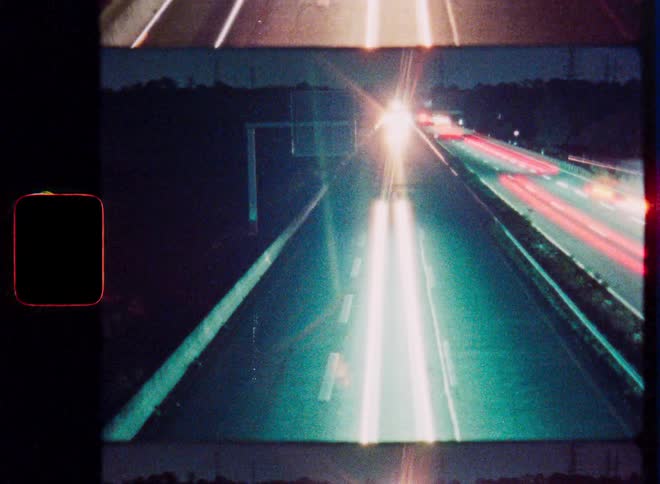 Vintage 8mm film captures a mesmerizing time-lapse of highway traffic at night with cars creating streaks of light