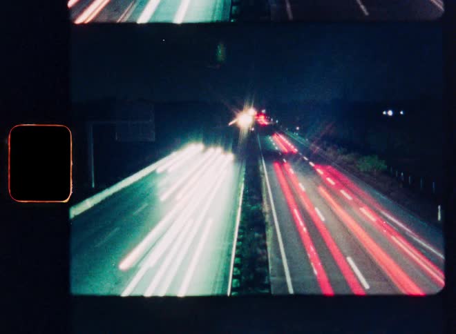 Retro-style 8mm film stop-motion shows a long exposure time-lapse of vibrant car light trails on a busy highway at night