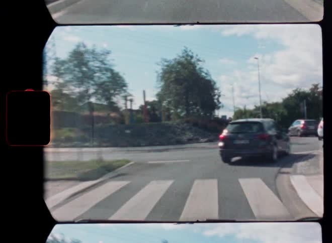 A vintage Super 8 film captures a driver's point of view while driving on a country road and into a small town