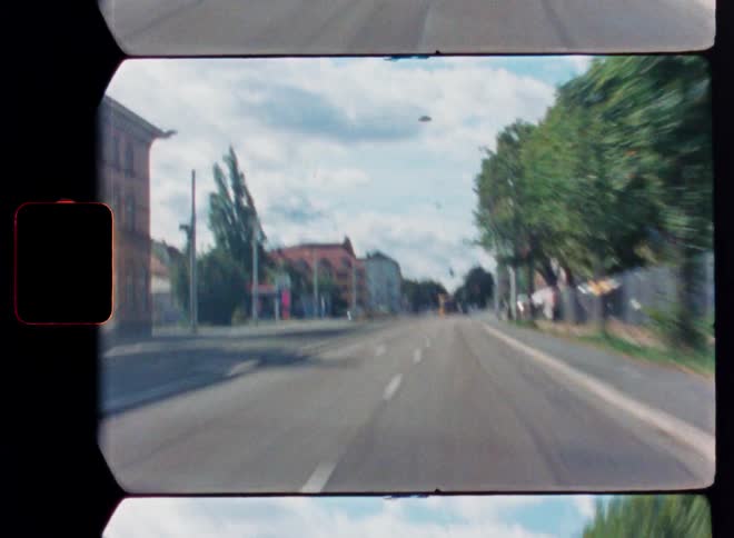 A vintage film perspective of driving through a European city street, passing a tram on a sunny day
