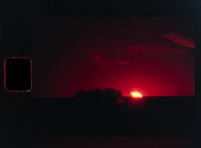 Archival Super 8mm footage captures a mesmerizing partial solar eclipse as it sets on the horizon, casting a deep red glow across the sky