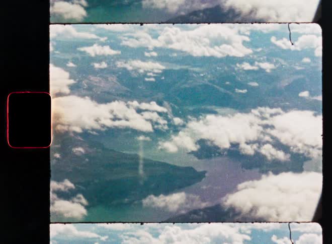 Scanned 8mm film footage shows a vintage aerial view of a mountainous landscape with a large lake and clouds