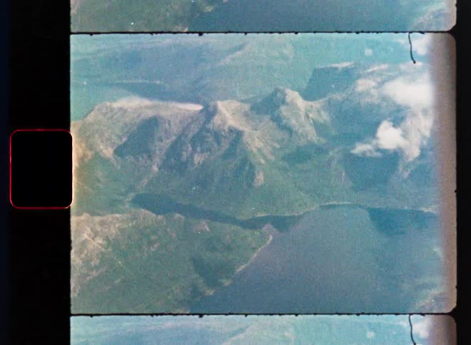 A nostalgic film scan captures a breathtaking aerial view of a majestic mountain range and a serene fjord