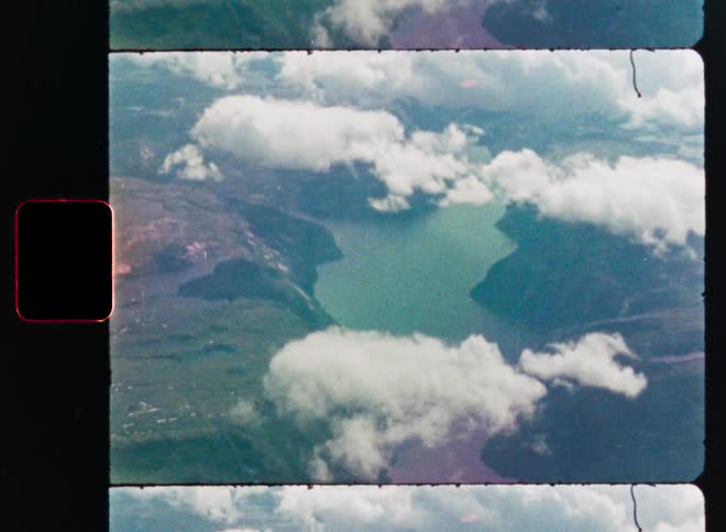 Authentic super 8mm film scan of an aerial view looking down at a mountain lake through the clouds