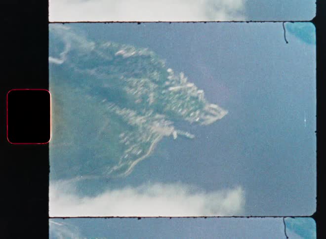 Vintage 16mm film scan captures an aerial view zooming through the clouds to reveal a coastal town with a harbor