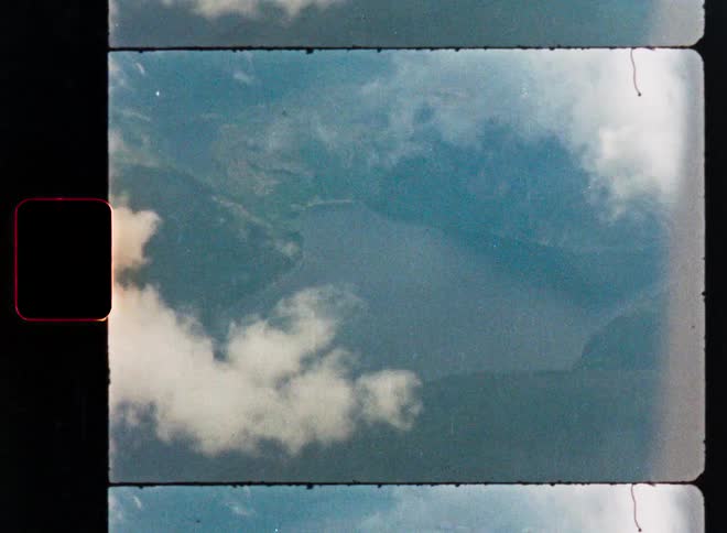 Vintage 8mm film scan shows a hazy aerial view of a mountain lake partially obscured by clouds