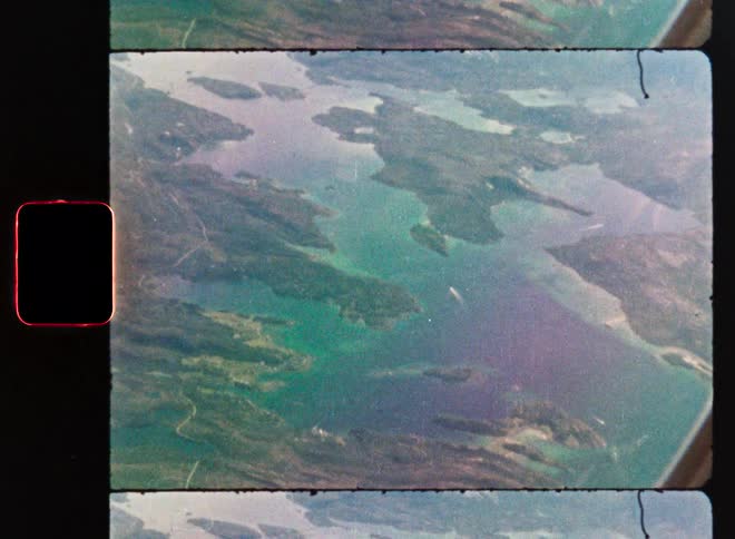 A vintage 8mm film captures an aerial view from an airplane of a beautiful archipelago with a boat sailing on the water