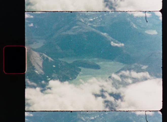 A Super 8 film scan shows a breathtaking aerial view of a mountain range and a serene lake seen through the clouds