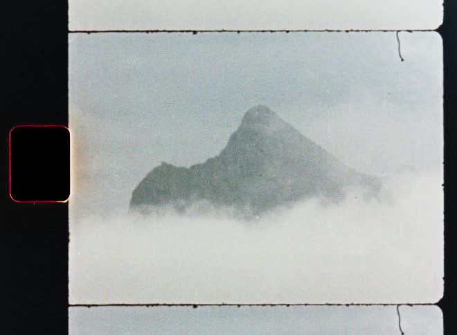 A vintage film strip scan captures a moody, atmospheric shot of a mountain peak above the clouds