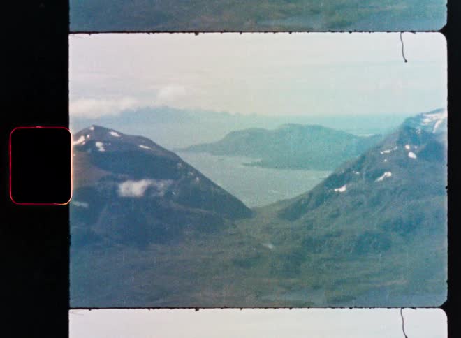 Vintage 8mm film footage captures a stunning aerial view of a majestic mountain range and expansive lake