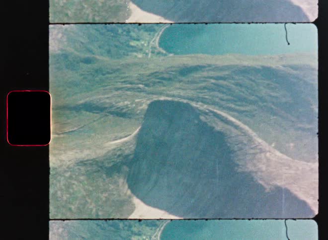 A vintage Super 8mm film captures a stunning aerial view of a majestic mountain rising over a serene fjord