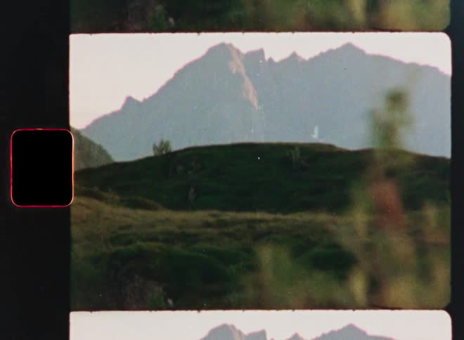 A vintage Super 8 film captures a view of rolling green hills with a majestic mountain range in the background