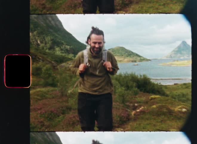 Vintage Super 8 footage captures a smiling man backpacking through a scenic green mountain landscape by a lake