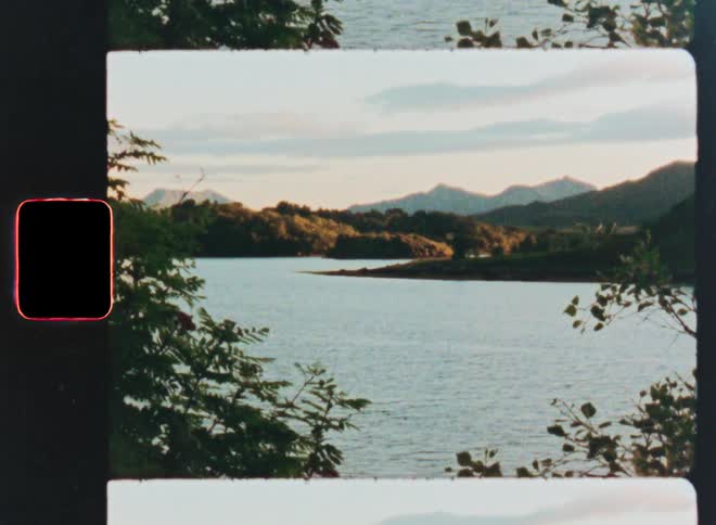 An authentic 8mm film scan captures a serene view of a tranquil lake surrounded by mountains at dusk