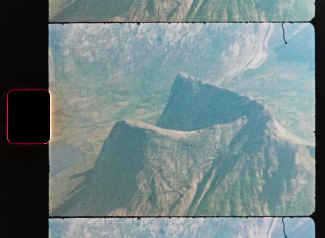 An aerial view from a vintage film scan reveals a majestic mountain rising beside a tranquil body of water