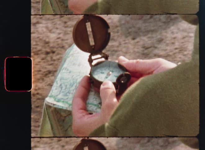 A close-up on vintage film shows a person's hands holding an old compass over a map to navigate