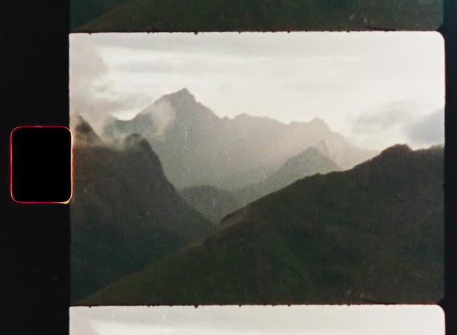 A moody and atmospheric vintage film scan shows a hazy and majestic mountain range with low-hanging clouds