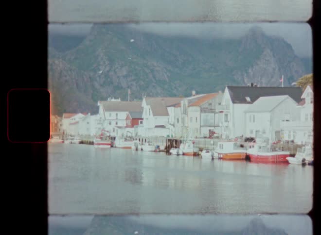 A tranquil Norwegian fishing village with boats docked along the waterfront and mountains in the background, captured on vintage film
