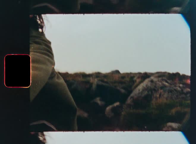 A smiling man reaches for the camera and leads the viewer on an adventurous hike through a rocky landscape in this vintage film-style clip