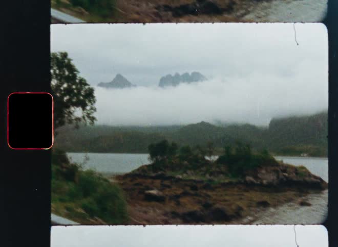A scenic drive along a lake reveals majestic mountains peeking through thick fog, captured on vintage 8mm film