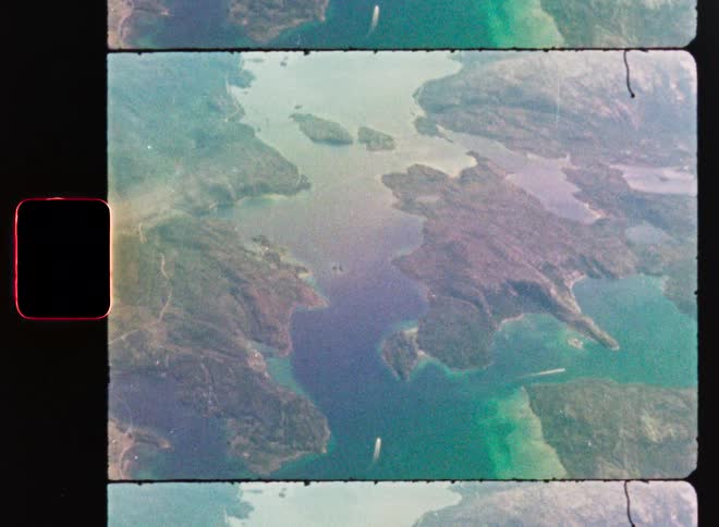 Aerial shot of green islands and turquoise water captured on a grainy, damaged vintage film strip
