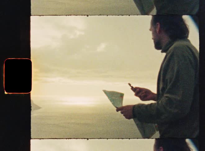 Authentic super 8 film footage of a man using a map and compass to navigate while overlooking a beautiful coastal view
