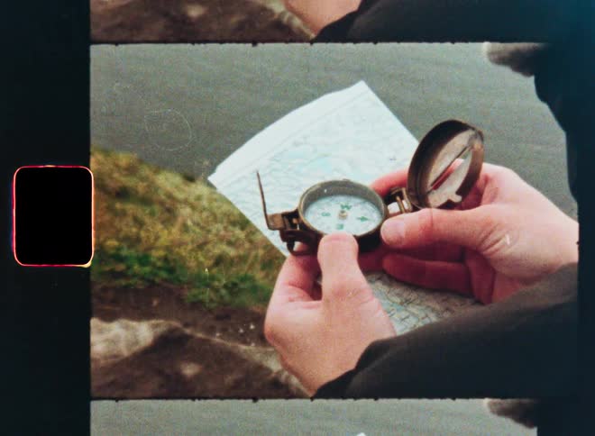 Close up on a person's hands holding a vintage compass and map while navigating on a cliff in this retro Super 8 film footage