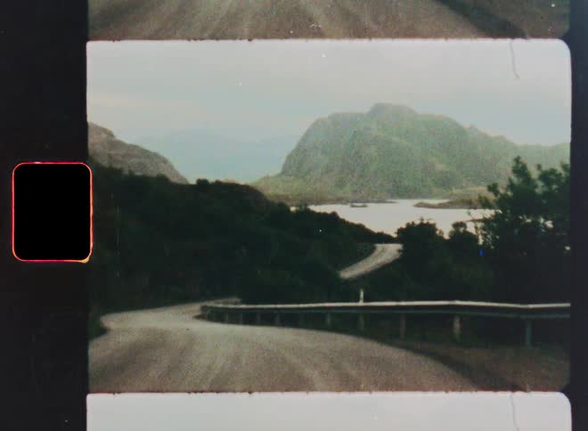 A vintage 8mm film captures a slow drive along a winding road through a beautiful mountain landscape in Norway