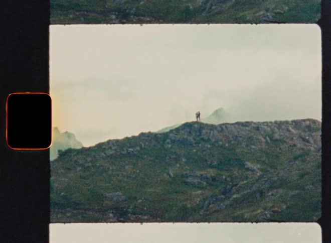 A vintage 35mm film scan shows two distant figures standing atop a misty mountain ridge, evoking a sense of adventure and nostalgia