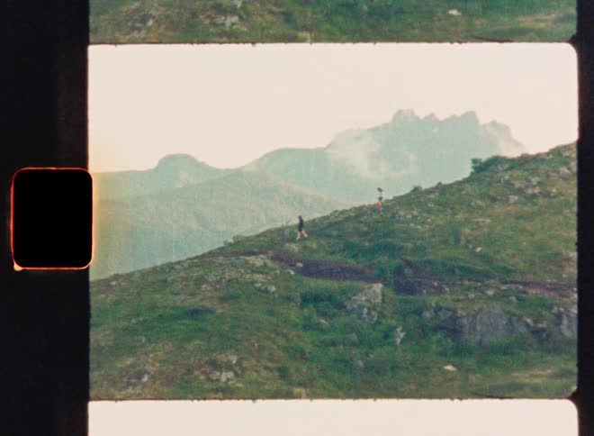 Vintage 16mm film scan shows two people hiking up a scenic green mountain path