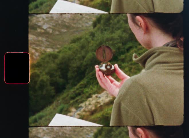 A female explorer checks her bearings with a map and an old-fashioned compass against a backdrop of green hills