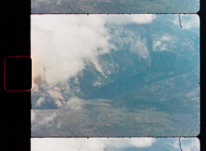 Vintage 8mm film strip of a majestic mountain range peeking through soft white clouds