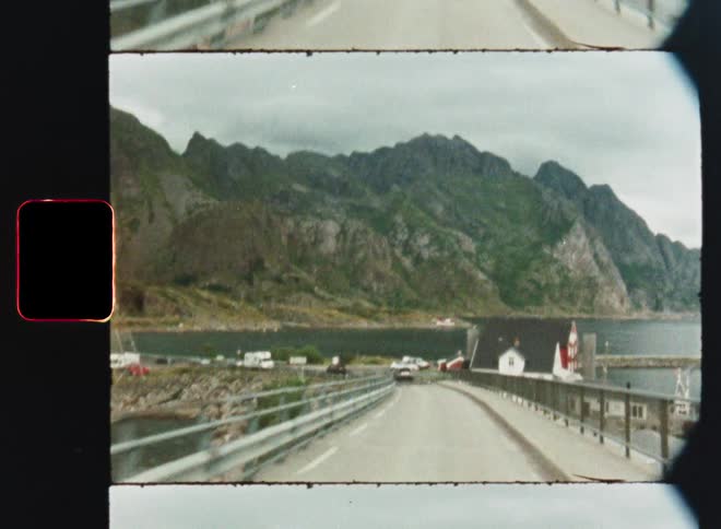 Vintage 8mm footage captures a scenic drive across a bridge towards a coastal Norwegian village and mountains
