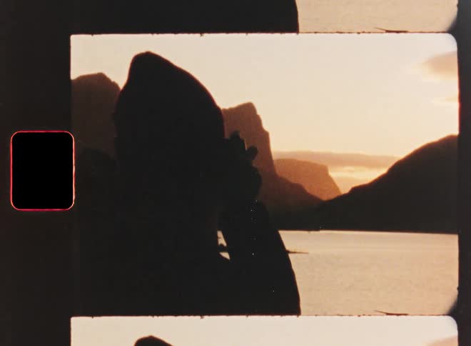 Silhouette of a photographer with a vintage camera captures the serene mountain and lake landscape at sunset