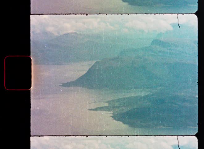 Vintage 8mm film scan of a hazy, aerial view over a mountainous coastline and water