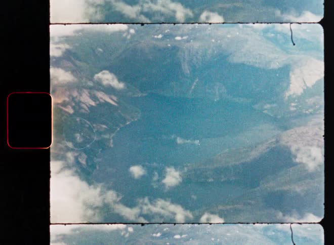 Scanned vintage film footage shows a breathtaking aerial view of a mountain lake surrounded by peaks and clouds