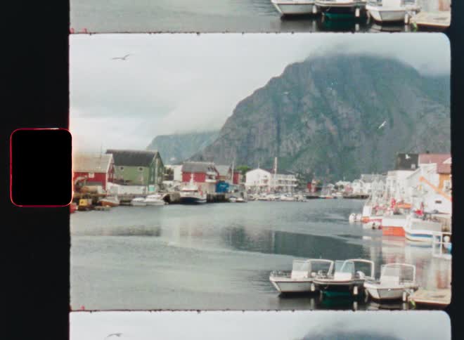 Vintage 8mm film captures a slow pan of a tranquil harbor town nestled at the base of a majestic mountain