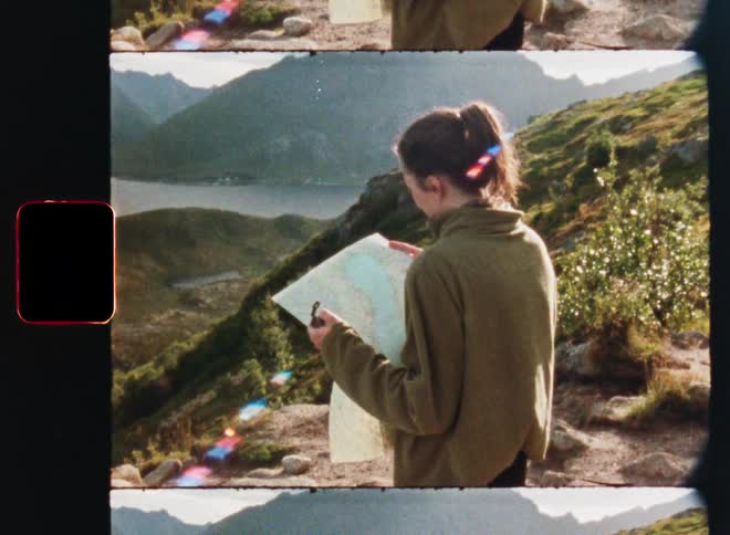 Vintage film footage shows a hiker with a map and compass overlooking a stunning mountain and fjord landscape